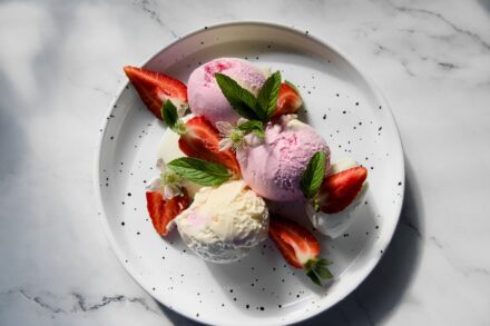 assiette sur laquelle sont posées 3 boules de glace et des morceaux de fraises ainsi que des feuilles en déco